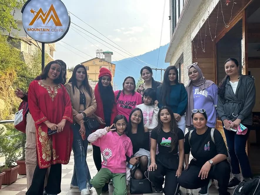 Eleven women and a young girl outside a guesthouse in the hills, gathered under a sign reading Mountain Cliffs, with pine slopes rising behind.