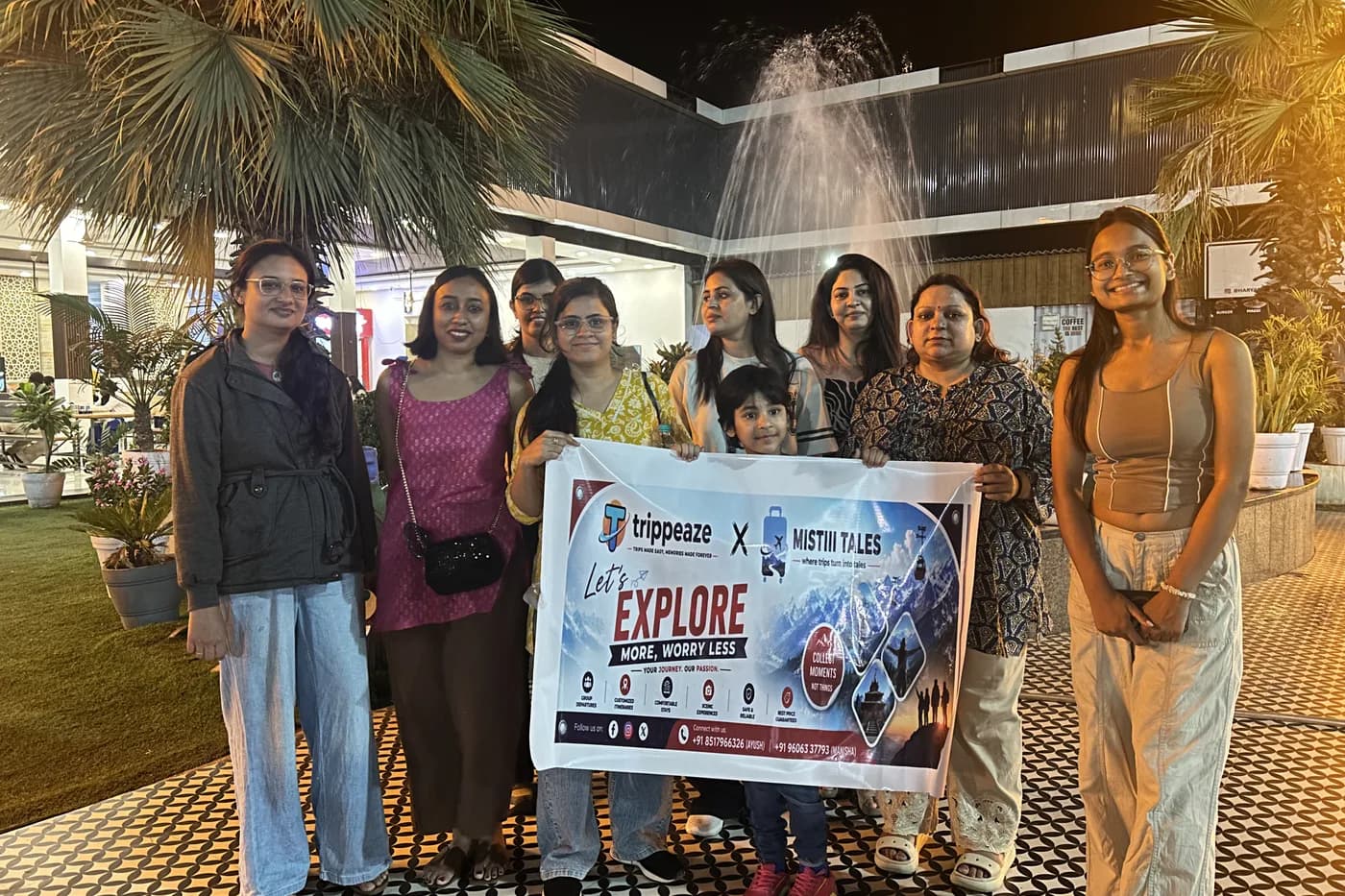 A travel group at night holding a banner reading 'trippeaze x Mistiii Tales — let's explore more, worry less'.